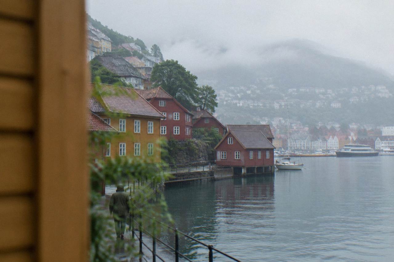 Old wooden houses painted ochre and red stacked on a hillside above a calm harbour in Bergen