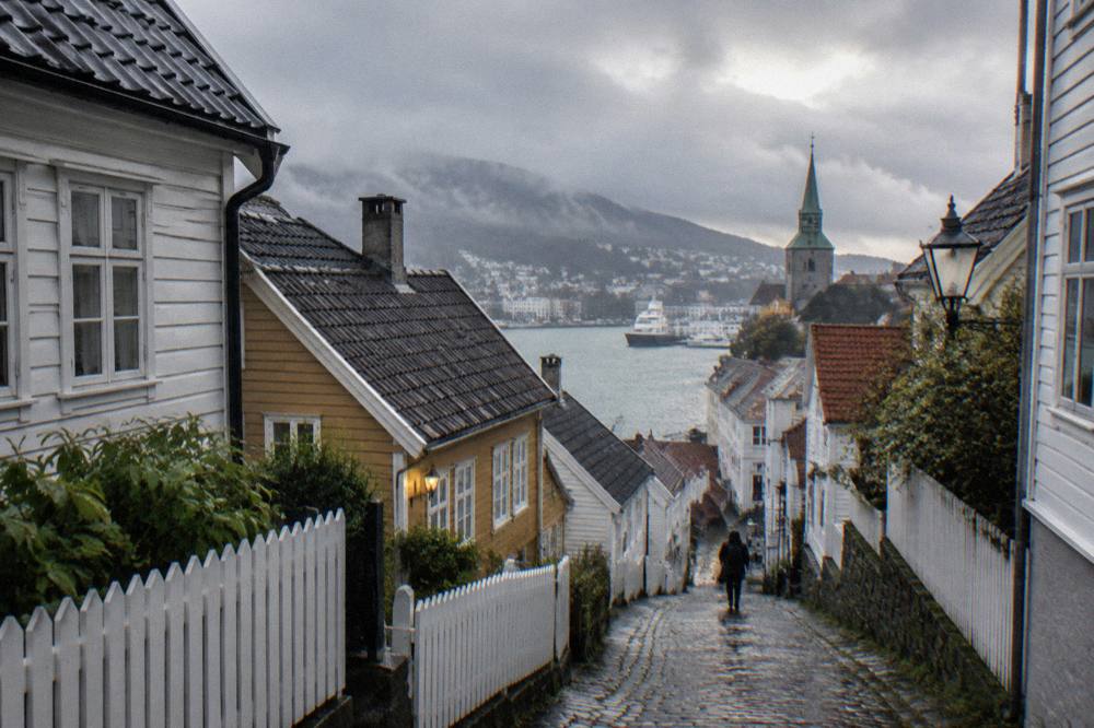 A quiet street of historic wooden houses with a church tower rising behind the rooftops