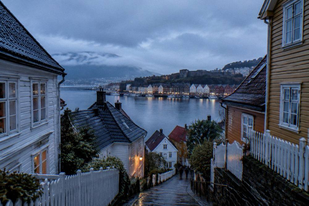 A stone fortress wall and historic harbour buildings seen across still water at dusk