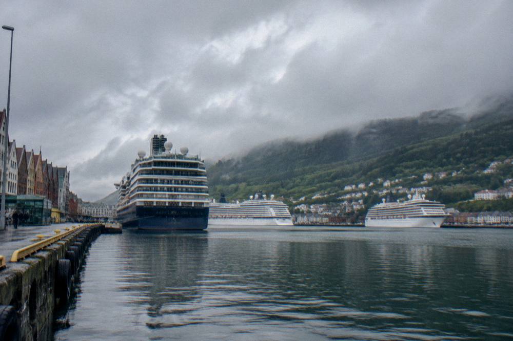 A harbour in Bergen with several cruise ships tied up at the docks below wooded hills
