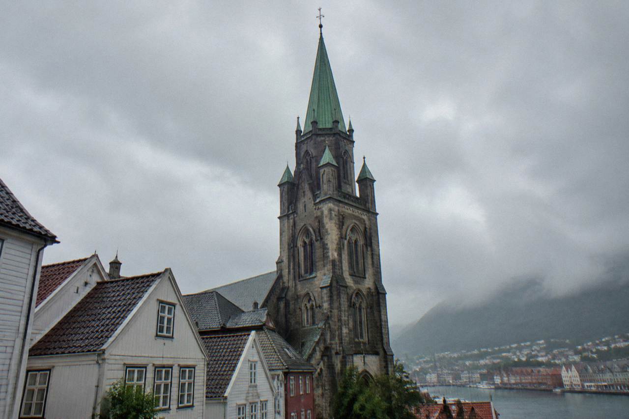 A stone cathedral with a tall tower rising above rooftops in the centre of a Norwegian coastal city