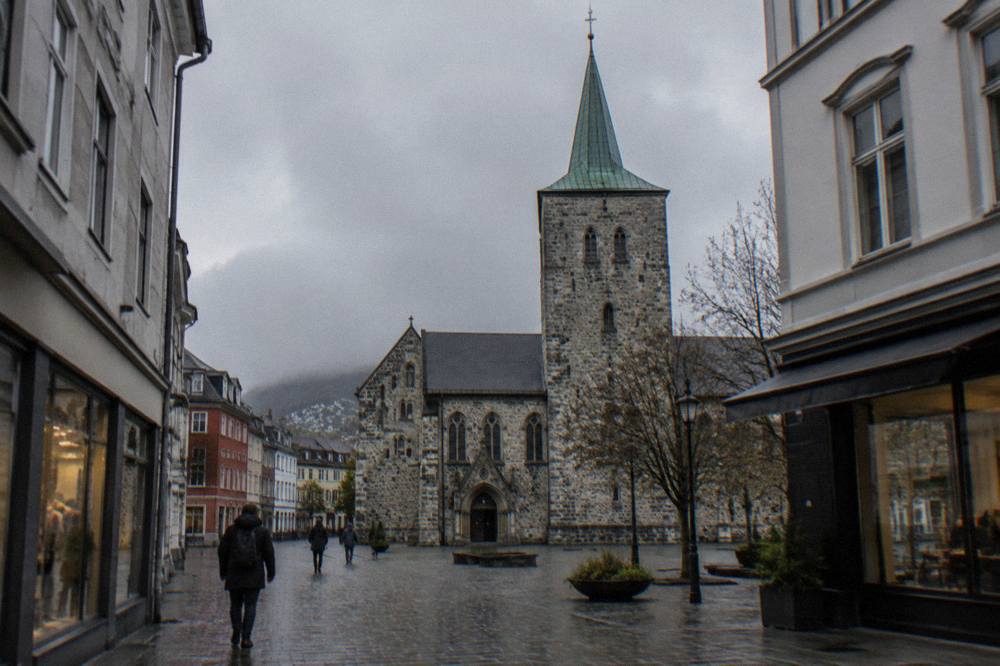 The stone tower and facade of a cathedral seen from a pedestrian street lined with shops