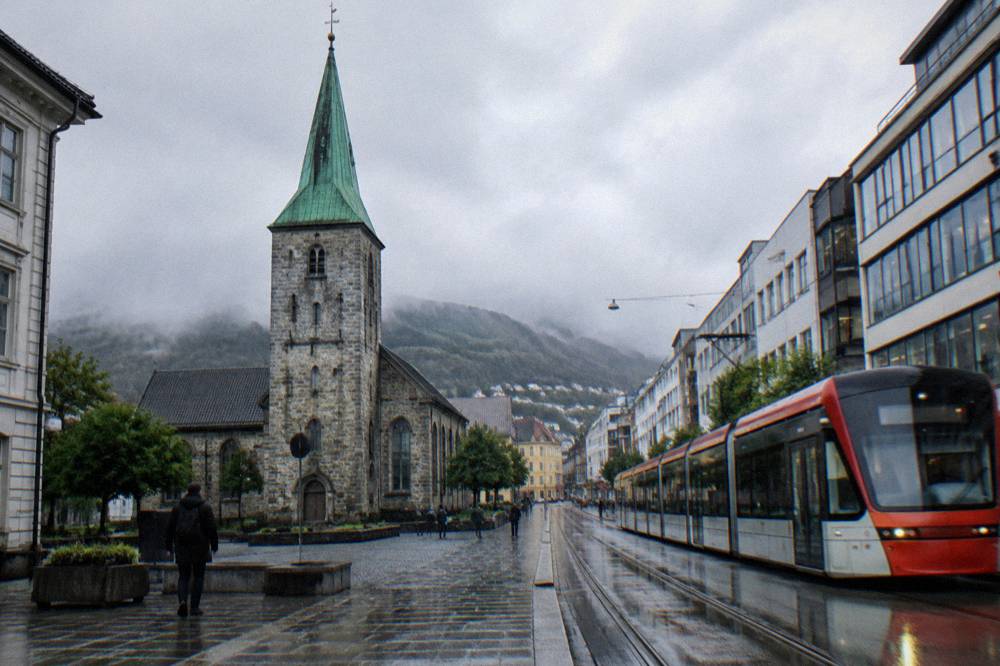 A light rail tram passing modern buildings on a street in a Norwegian city