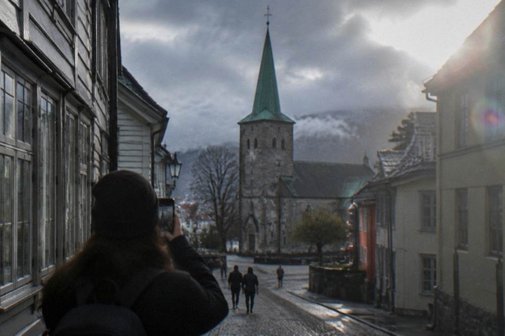 A tourist holding a smartphone while looking at historic buildings on a narrow street