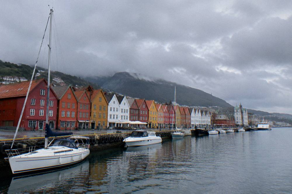 Colorful wooden buildings along a historic wharf beside a harbour with boats moored nearby