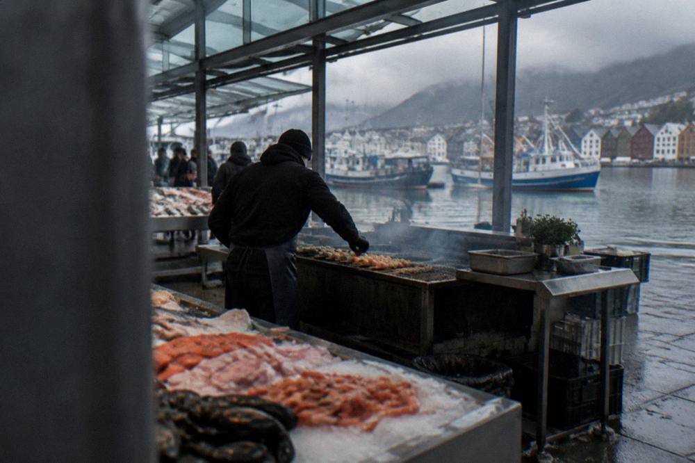 A cook placing skewers on a grill at a busy market stall