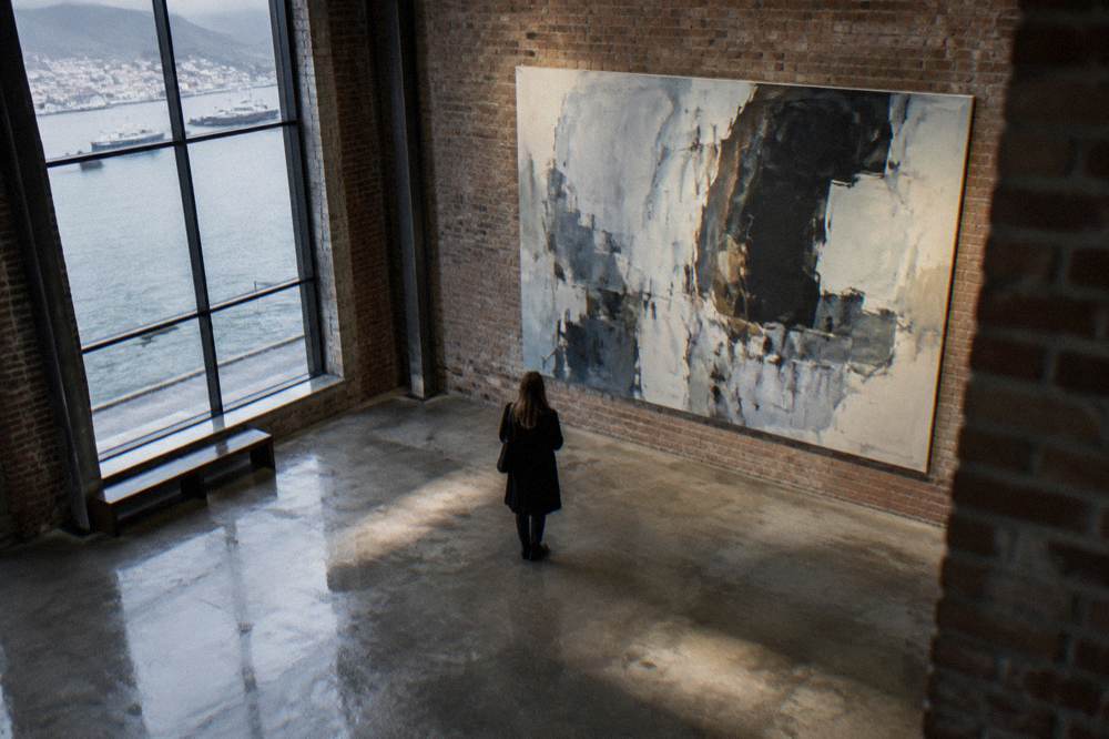 A gallery visitor standing before a large abstract artwork in a converted harbour building with visible brick