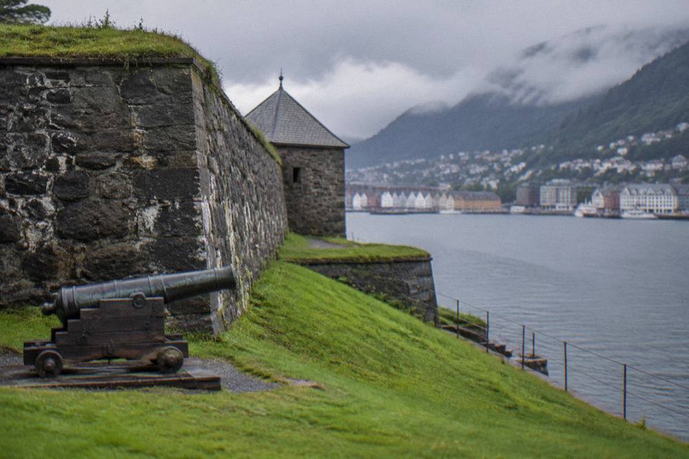 A stone fortress wall and green lawn beside a narrow sea inlet in a Scandinavian city