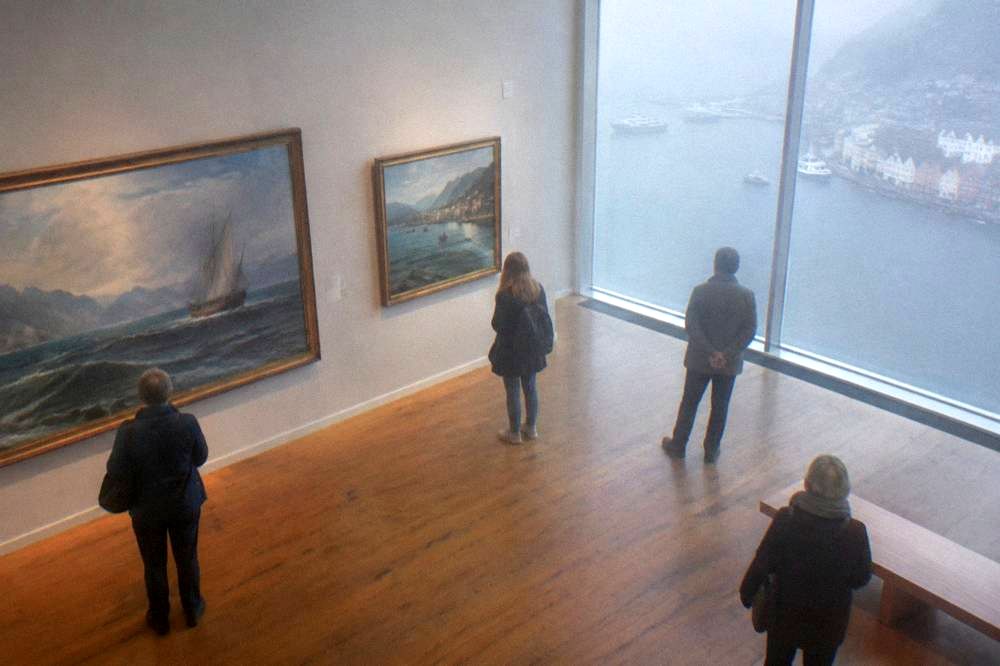 Visitors looking at maritime paintings in a gallery with wooden floors in Bergen