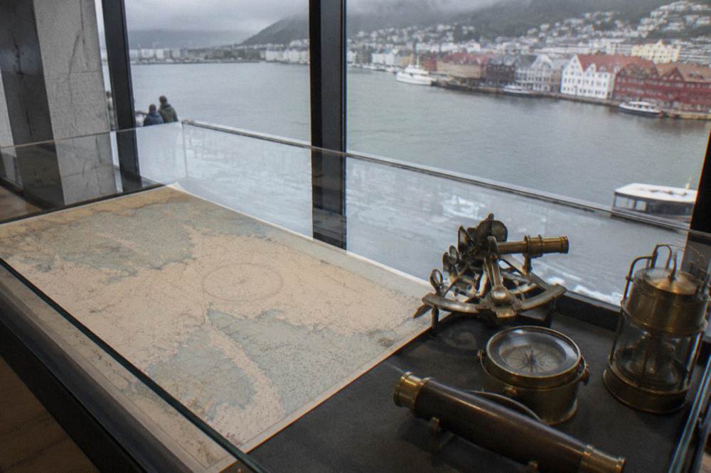 A nautical chart and brass instruments displayed in a museum case in Bergen