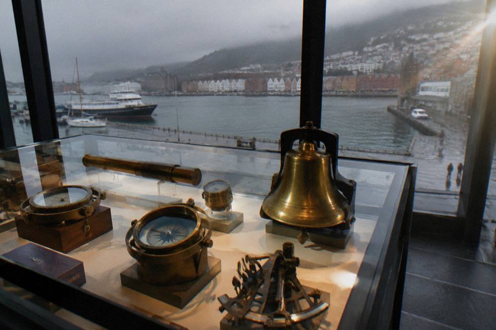 Old nautical instruments and a ship bell displayed in a lit case in Bergen