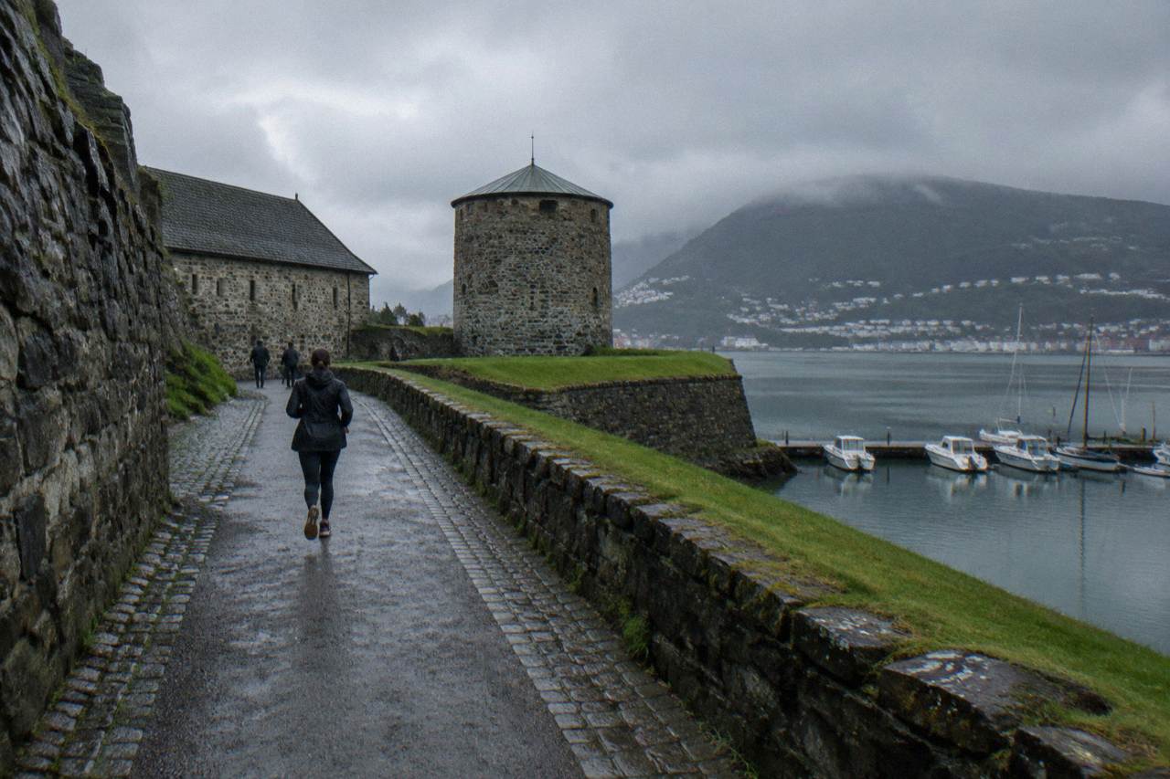 Stone walls and a round tower of an old fortress beside a harbour with small boats moored in front