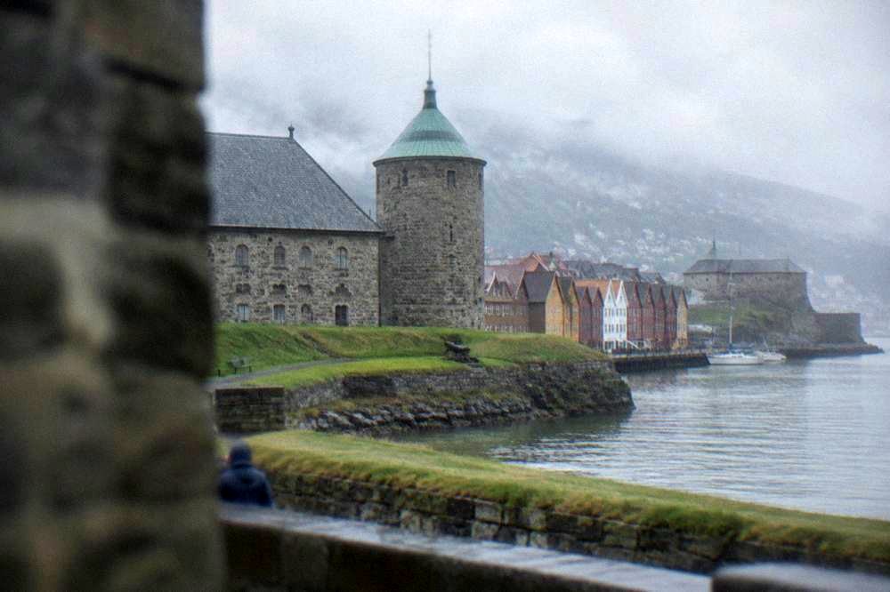 Colourful old wooden trading buildings along a wharf with a stone fortress visible beyond