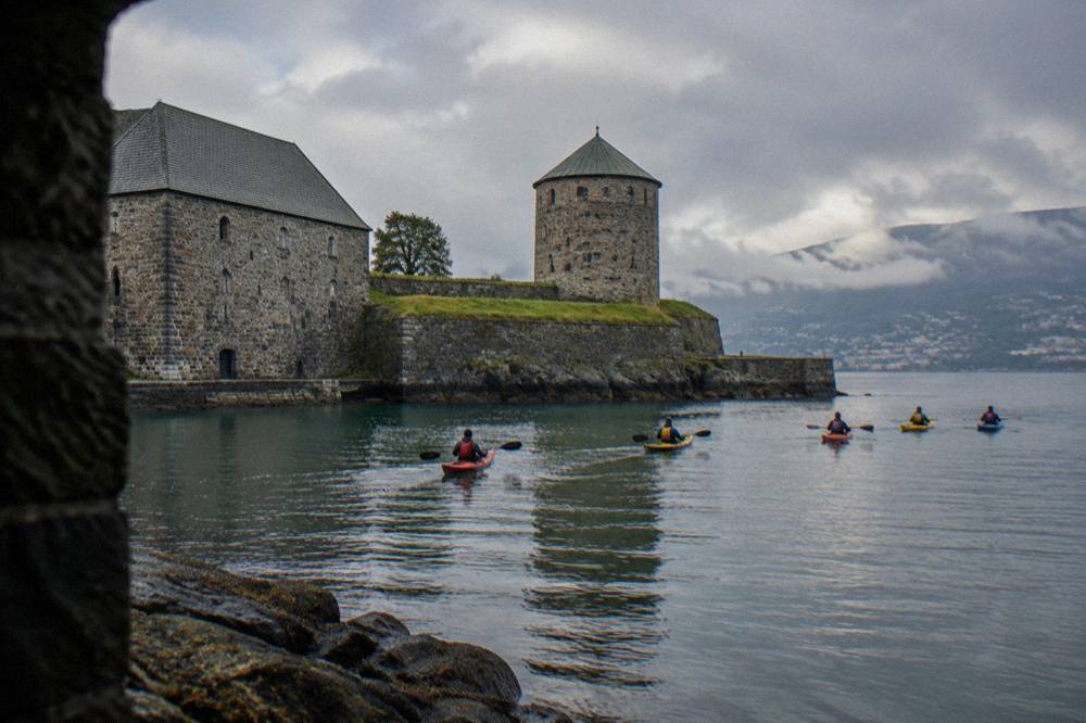 A group of kayakers paddling small kayaks on calm water near a rocky shoreline