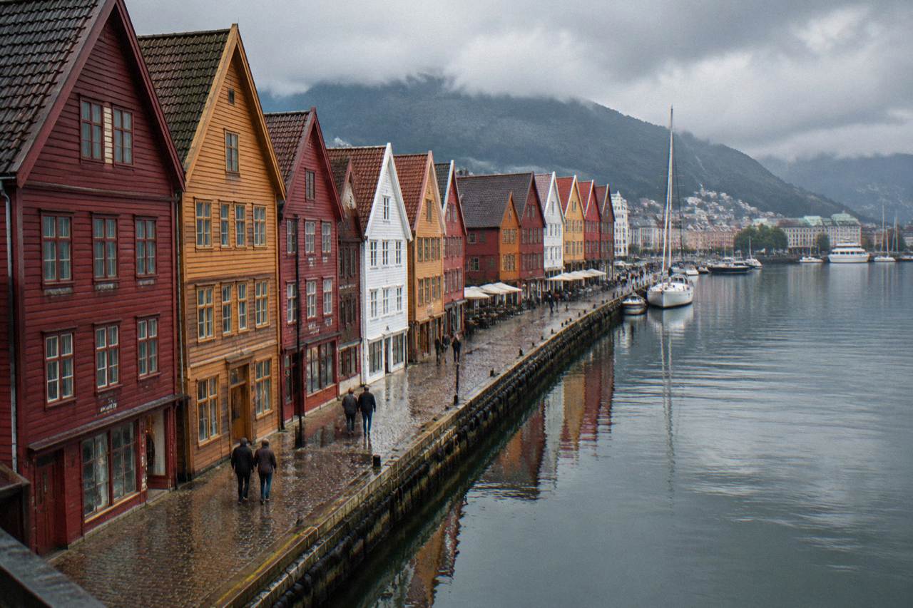 Colourful wooden trading houses of Bryggen standing along the harbour in Bergen, with the wharf reflected in still water.