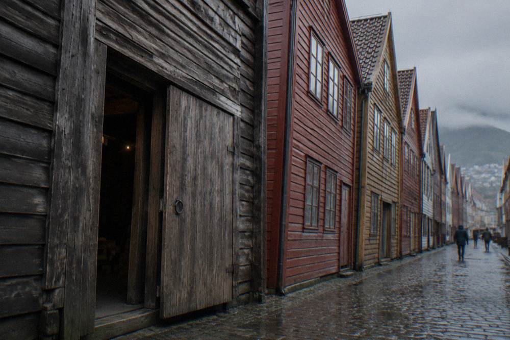 A wooden warehouse door on Bryggen standing slightly ajar, with rough plank walls and aged timber framing.