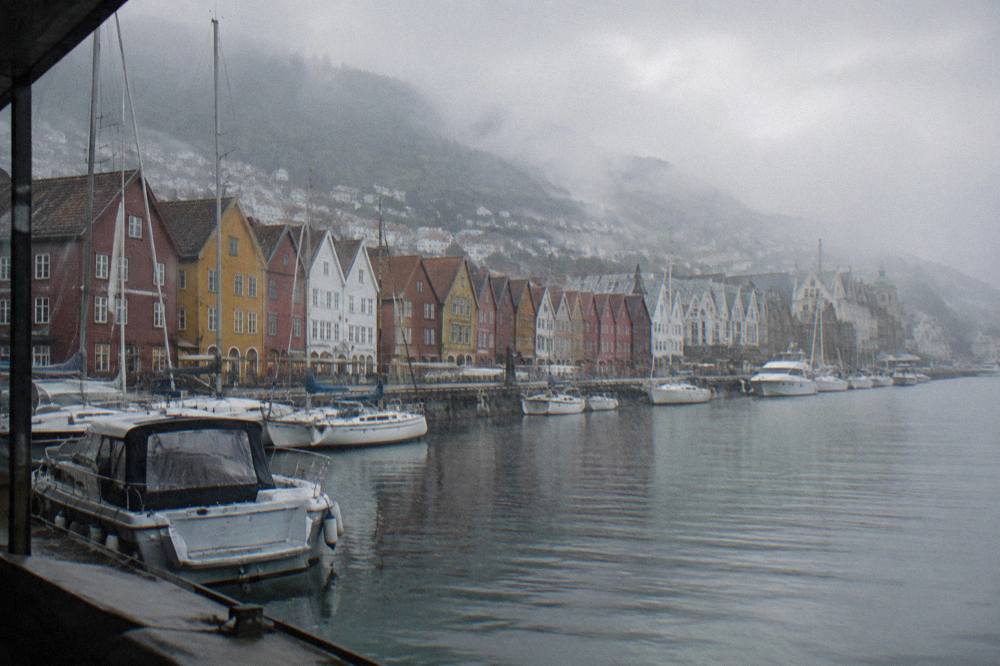 View along the length of Bryggen's wharf, with a line of gabled warehouse facades facing the water and boats in the foreground.