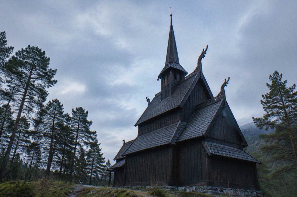 A view up the side of the wooden church showing three roof tiers and a carved gable ornament against the sky