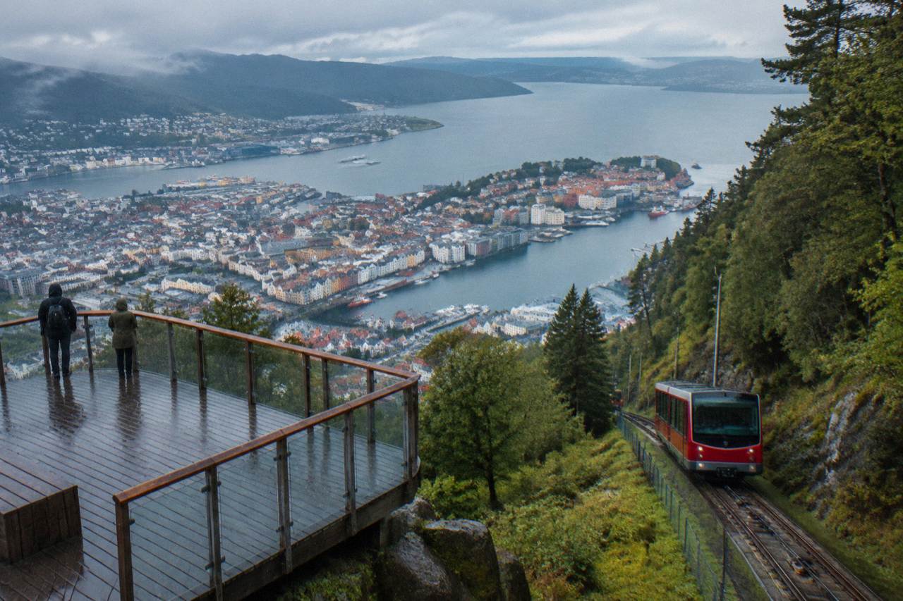 Red funicular cars climbing the wooded slope of Mount Floyen above Bergen's colourful harbour buildings