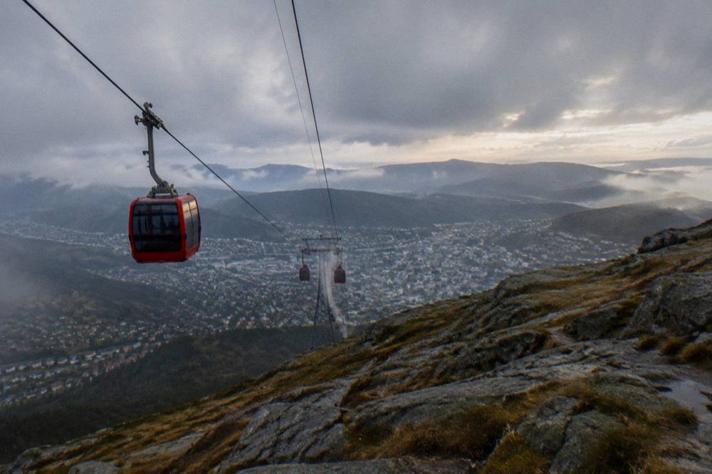Aerial gondola cabins of the Ulriken cable car rising above Bergen's city rooftops seen from a distance