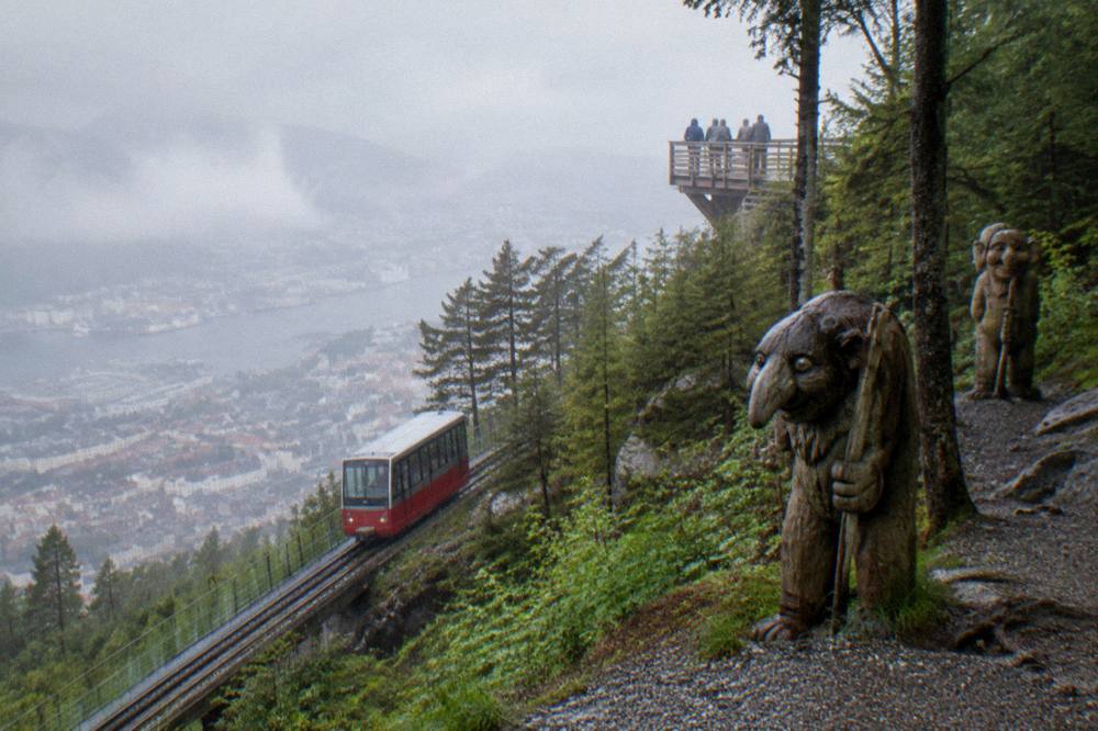 Wooden carved troll figures standing among trees on a forest path below the Floyen upper station