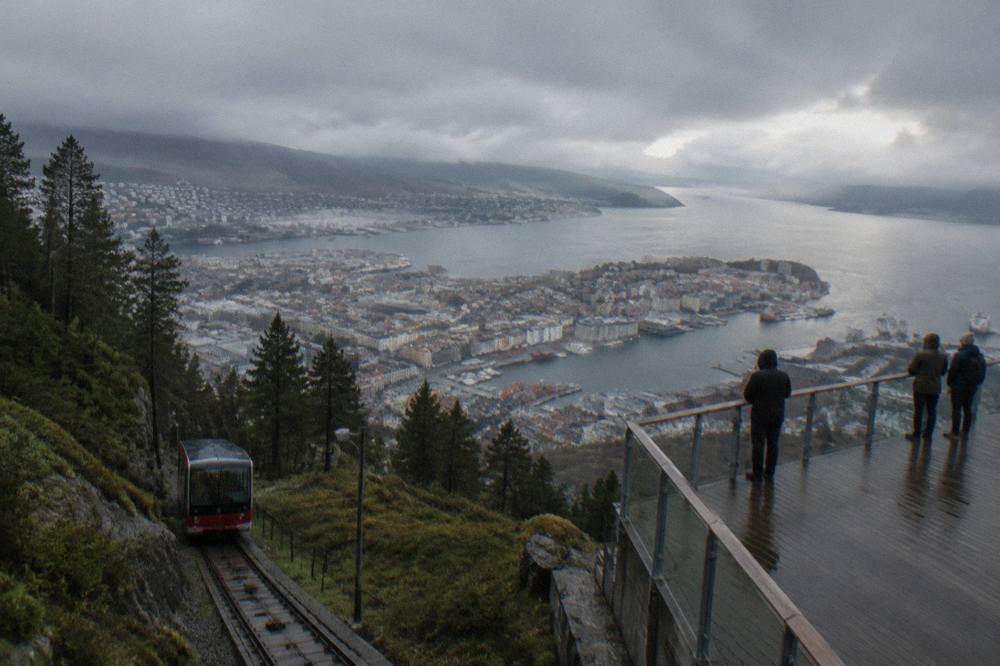 Evening light over Bergen rooftops and harbour from the Floyen viewing terrace with few people on the platform