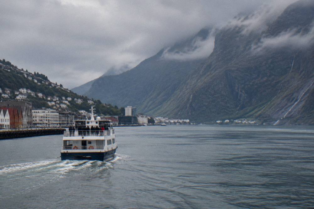 Tour boat heading out from Bergen harbour toward steep fjord cliffs