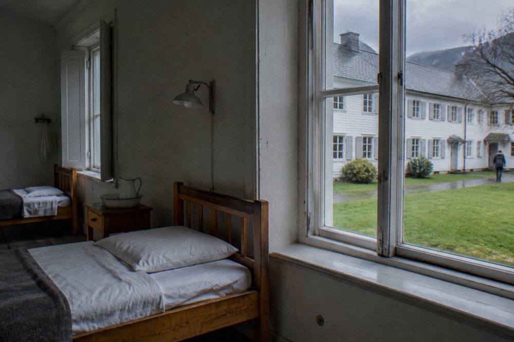 A sparse hospital ward room with simple wooden beds and whitewashed walls