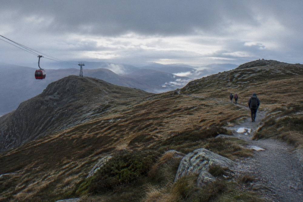 Hikers on a narrow gravel path crossing open moorland between two mountain tops