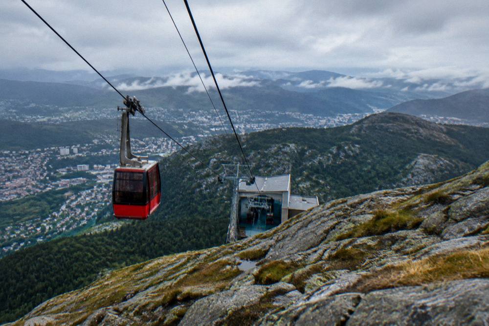 A cable car cabin descending toward a station with forest and city buildings below