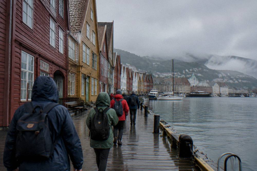 A small group of walkers following a guide along a historic wharf of coloured wooden buildings in Bergen