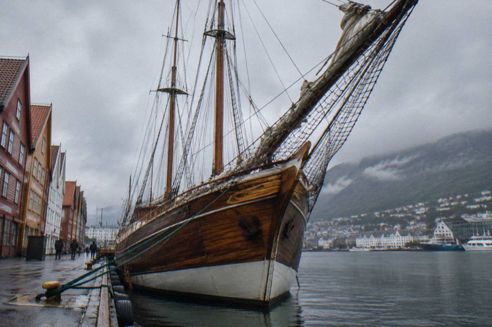 A historic wooden sailing ship moored beside old wharf buildings in Bergen harbour