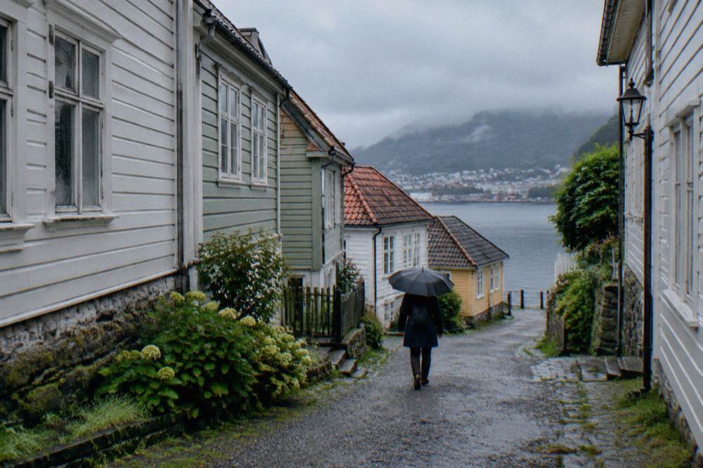 A visitor walking a gravel path between old wooden museum buildings in light rain