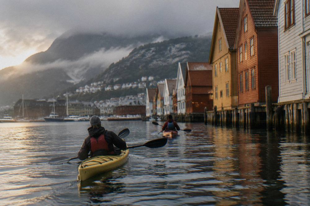 Kayakers paddling on calm water past a wooden Bergen shoreline