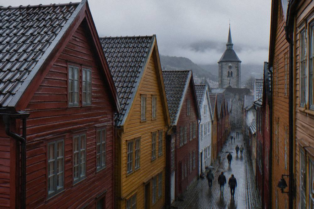 Narrow wooden lane between Bryggen warehouses leading toward a grey stone church tower