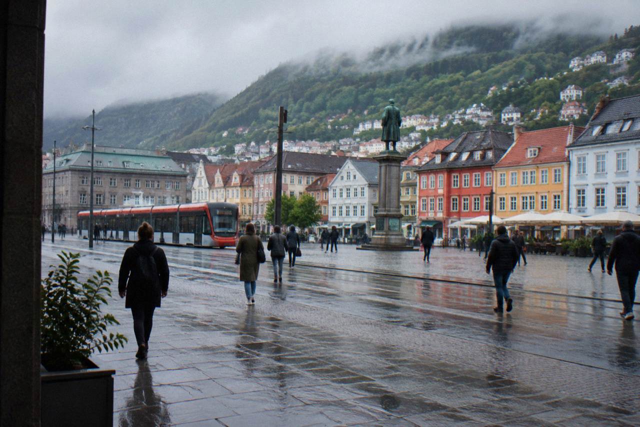 The open main square of Bergen city centre with its statue column and people crossing between colourful shop fronts