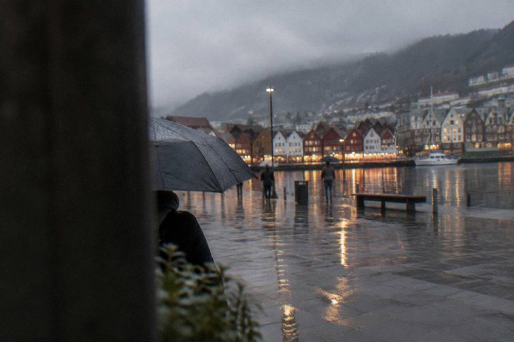 Rain-soaked paving and reflections of shop lights on a city square in Bergen in the evening