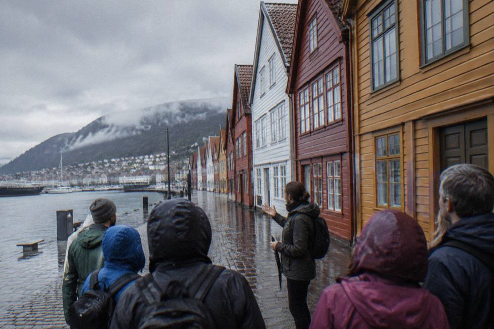 A guided walking group listening to a guide beside historic wooden buildings in central Bergen