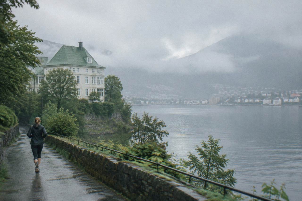 A pale wooden villa with a green roof standing above a calm lake, with trees along the shoreline