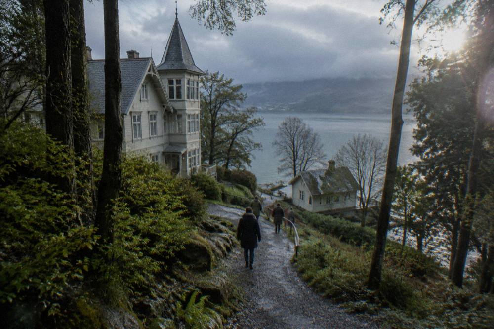 Visitors walking on a gravel path between trees toward a lakeside house