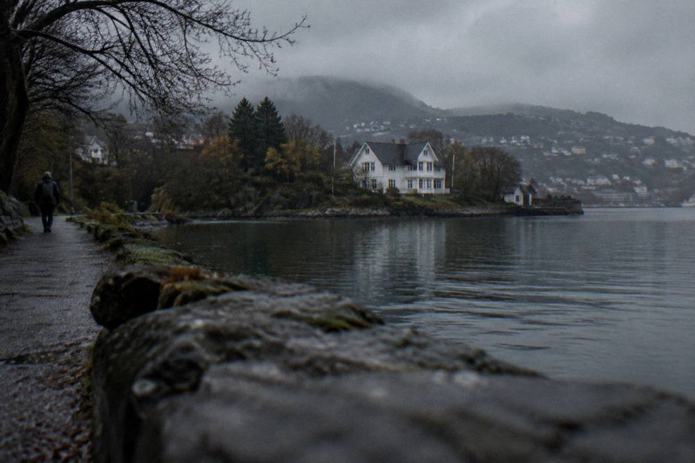 A wooden villa seen across a lake from a shoreline path in soft evening light