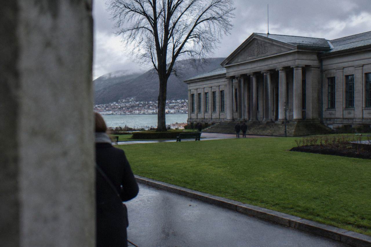 A large stone museum building with columns and a lawn in front, under a grey sky in Bergen.