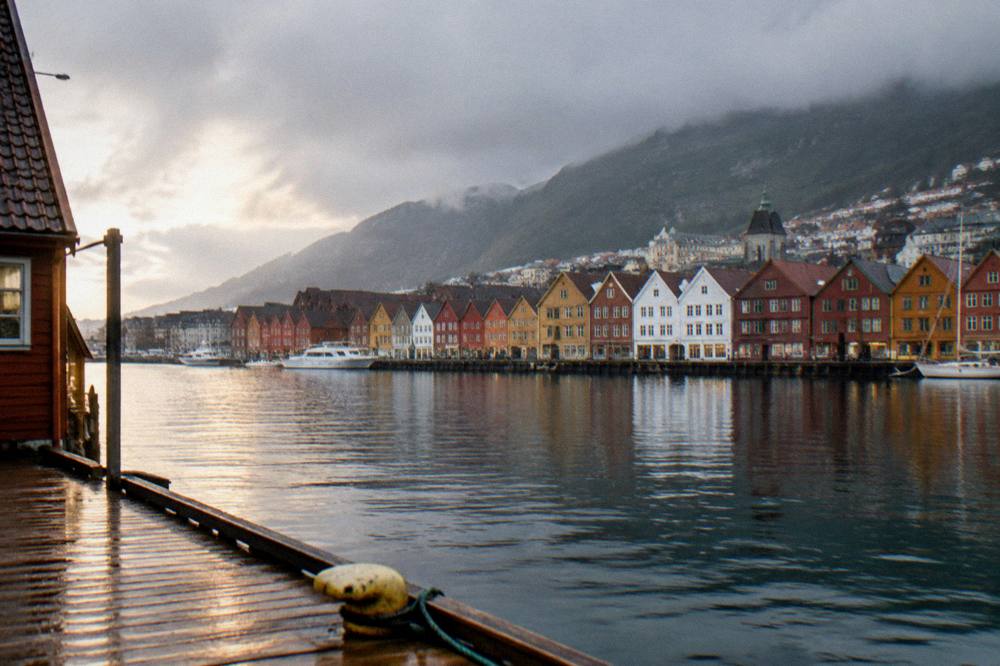 A wooden wharf with colorful gabled buildings along the waterfront in Bergen, seen across a harbor.