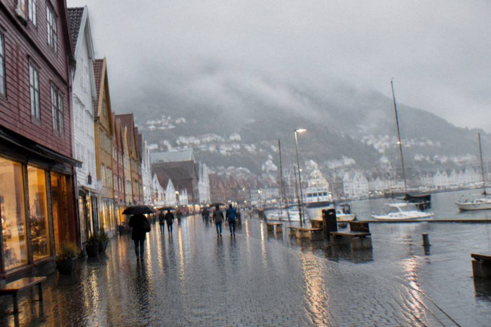 A rainy street in Bergen with wet cobblestones reflecting the lights of shop windows.