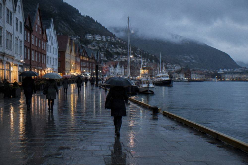 A rainy street scene in central Bergen with people walking under umbrellas