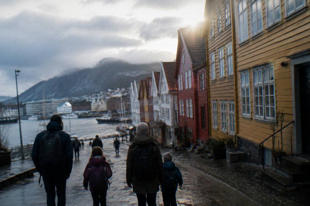 A family with backpacks walking through central Bergen past colorful wooden buildings