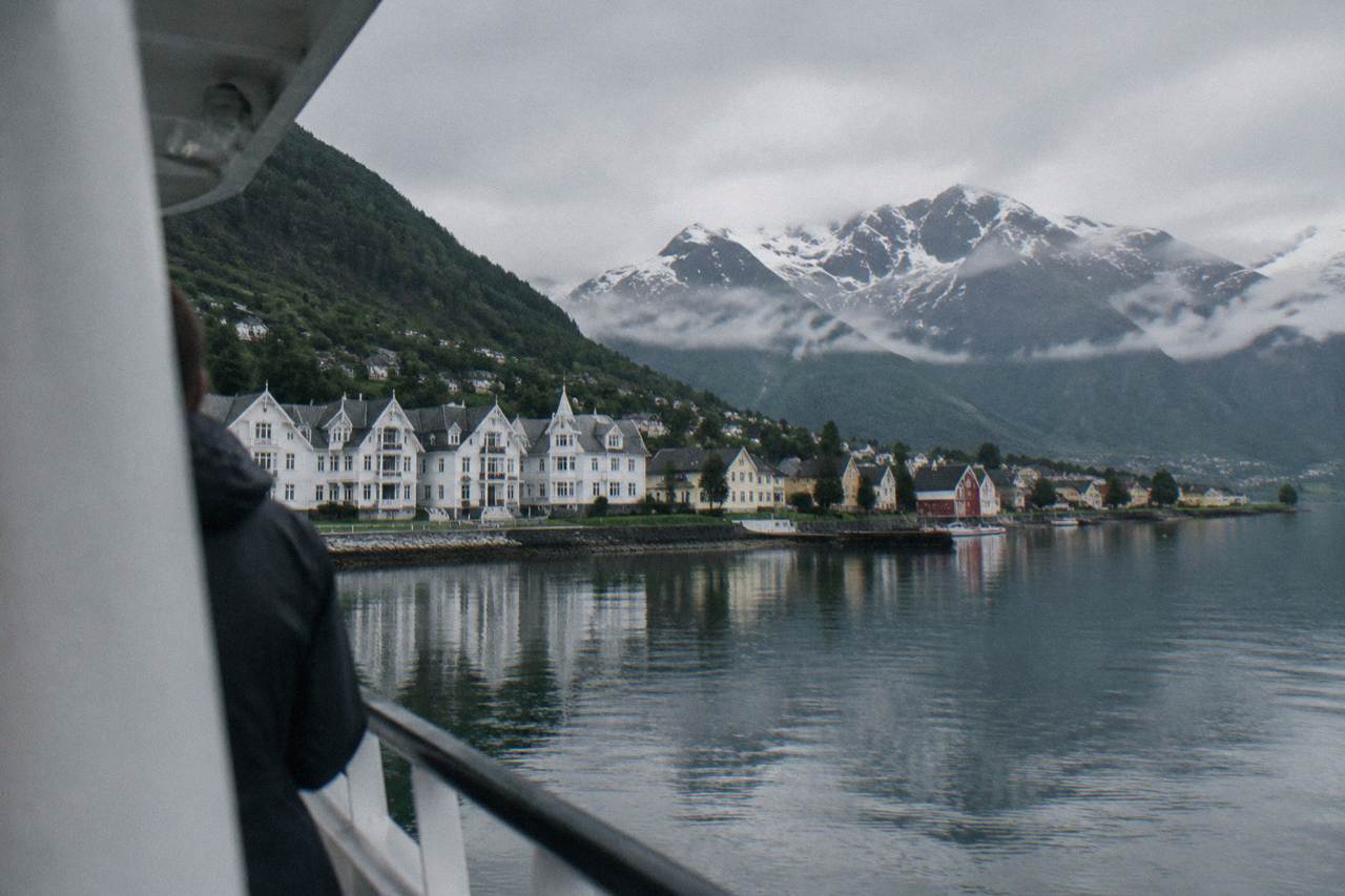 A small village of coloured wooden houses standing at the edge of a still fjord, steep forested mountains rising behind them