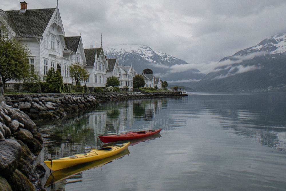 Two kayaks floating on calm fjord water close to a rocky shore, mountains reflected in the surface