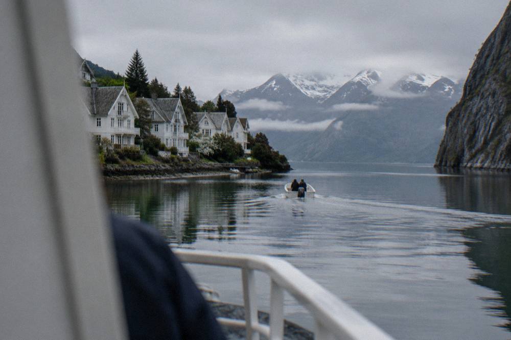 A small open boat crossing a narrow fjord passage with rock walls rising on both sides
