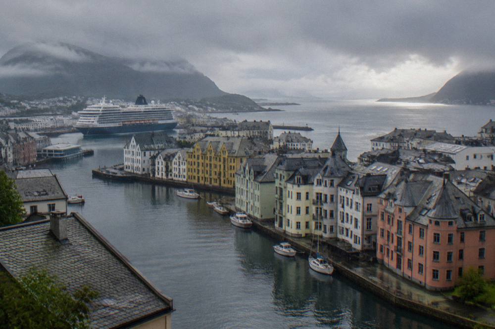 A cruise ship docked in a small Norwegian harbor town surrounded by steep hills